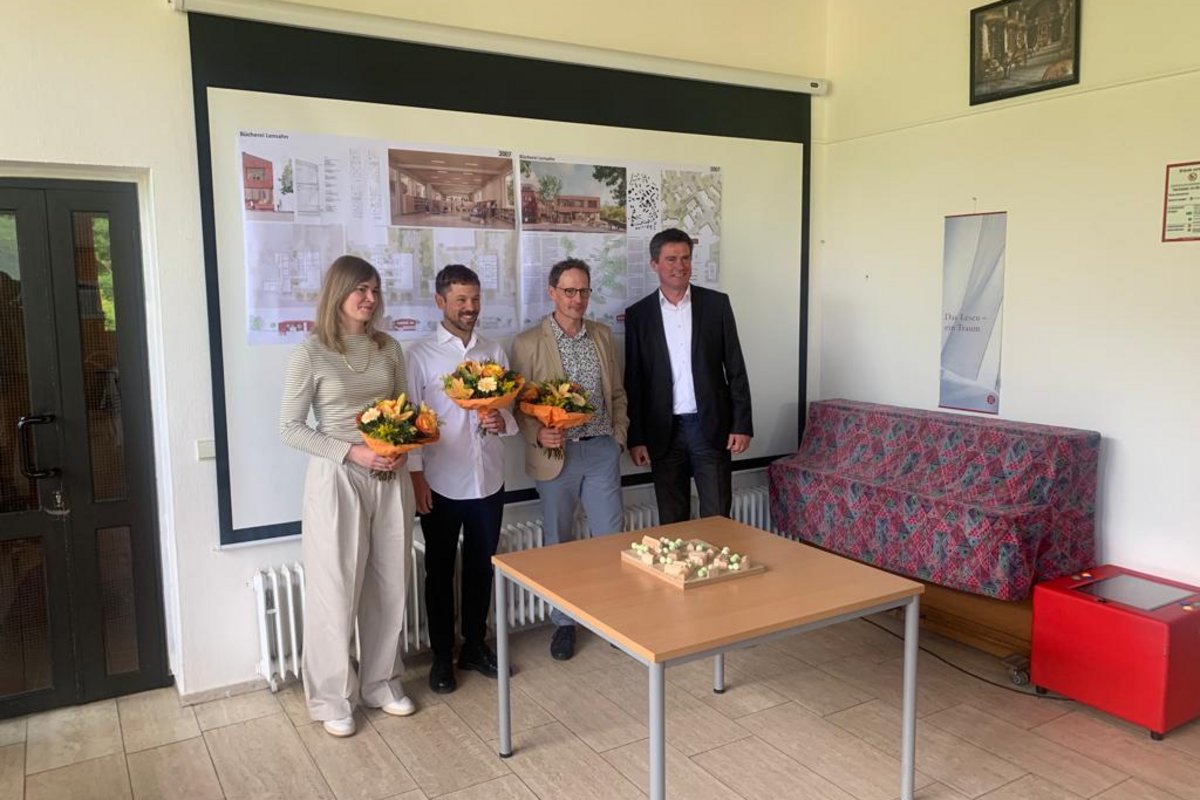 Bürgermeister Michael Robien mit den Gewinnern des Architektenwettbewerbes posieren für ein Foto in der Bücherei