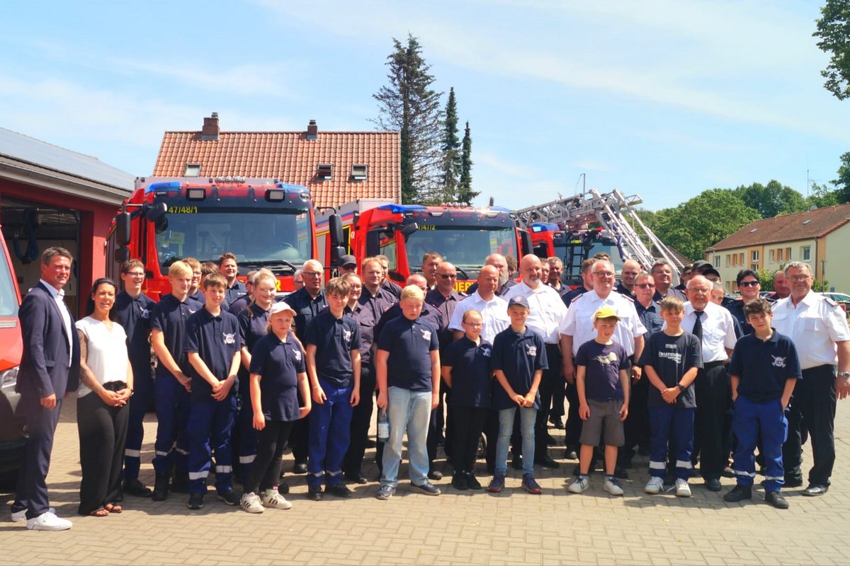 Feuerwehrmitglieder stehen vor den Feuerwehrfahrzeugen auf dem gepflasterten Vorplatz des Feuerwehrhauses