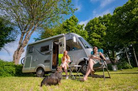 Zwei Frauen und ein Hund sitzen vor einem Campingwagen auf dem Wohnmobilstellplatz
