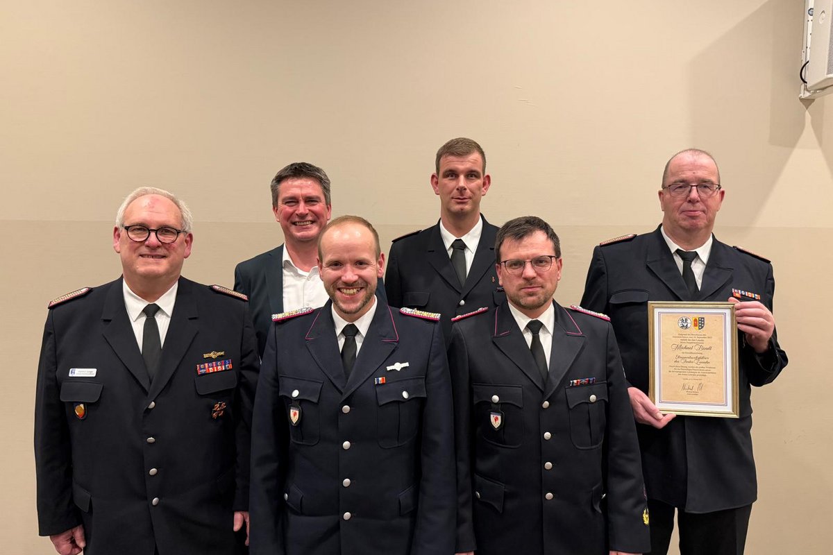 Bürgermeister Robien, Ehrenamtswehrführer Michael Bendt und weitere Personen posieren für ein Foto vor einer weissen Wand