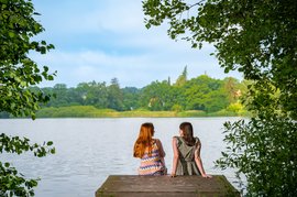 Zwei Frauen sitzen am Steg mit Blick über den Mühlenteich